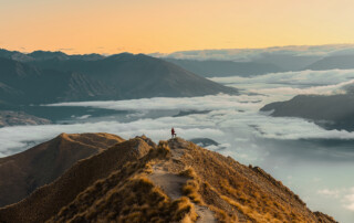 Frau auf einem Gipfel blickt in einen goldenen Himmel